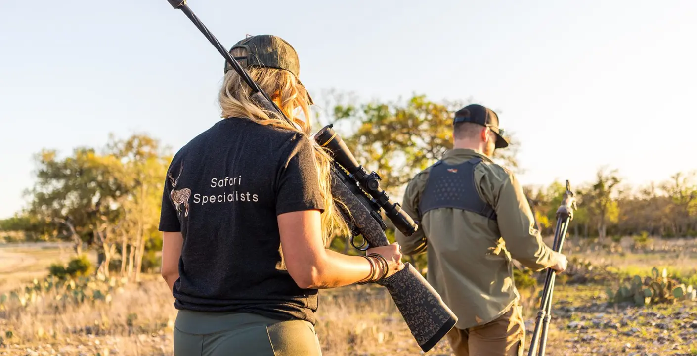 A hunter walking with a rifle across West Texas country