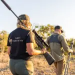 A hunter walking with a rifle across West Texas country