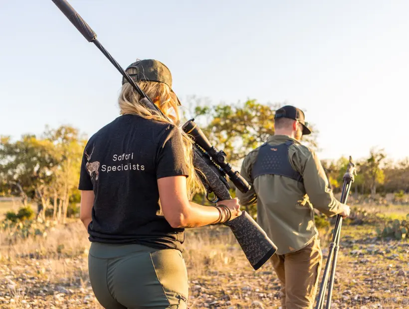 A hunter walking with a rifle across West Texas country