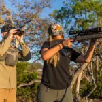 A hunter on shooting sticks and a guide glassing in the Hill Country brush