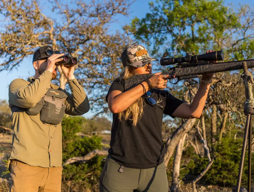 A hunter on shooting sticks and a guide glassing in the Hill Country brush